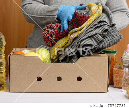 woman in gloves keeps collecting food, fruits and things and a cardboard box for helping those in need woman in gloves keeps collecting food, fruits and things and a cardboard box for helping those in need 75747785