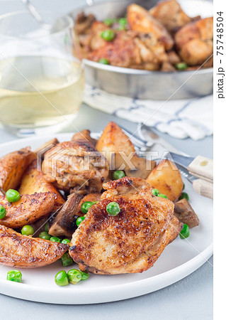 Chicken with potatoes, mushrooms and green peas, on a white plate and in metal pot, vertical 75748504