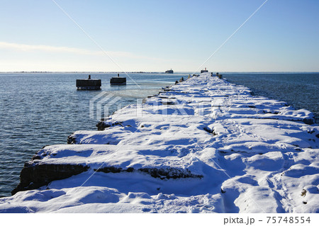 winter seascape, port entrance with snow covered concrete breakwater 75748554