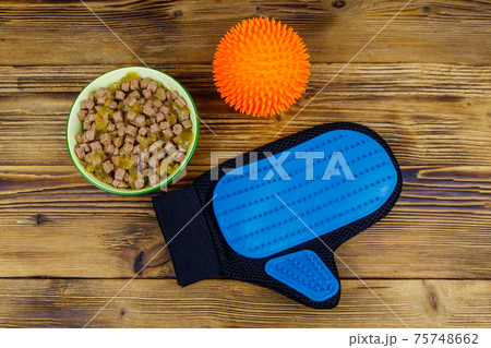 Canned dog food in bowl, ball toy and pet grooming glove on wooden background. Top view. Pet care concept 75748662
