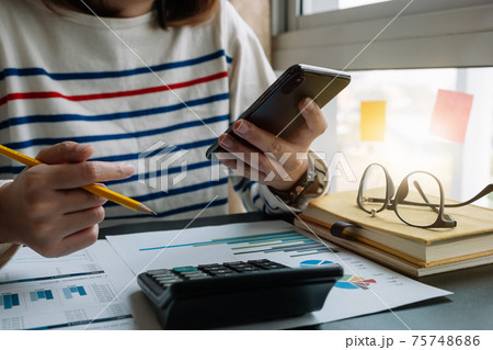 Close up of accountant hand holding smartphone while working on calculator to calculate financial data report,  75748686