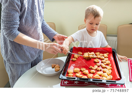 Back view young adult mother learn cooking sweet tasty cookies cute little toodler boy kid at home kitchen. Mom with small son baking sweet pastry homemade dessert. Parent child together activity 75748897