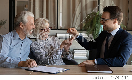 Smiling male relator give keys to senior couple buyers Smiling male relator give keys to senior couple buyers 75749114