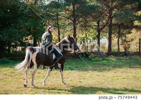 On a warm autumn day, a young girl went out to ride her mare on horseback around the farm On a warm autumn day, a young girl went out to ride her mare on horseback around the farm 75749443