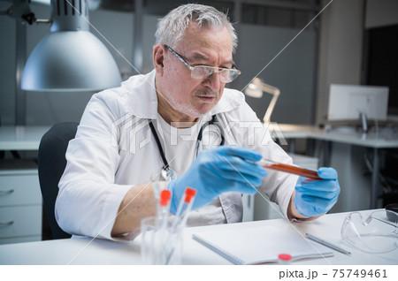A medical laboratory assistant examines the properties of the vaccine produced. He holds a bottle with a blood sample containing a vaccine against the covid-19 virus A medical laboratory assistant examines the properties of the vaccine produced. He holds a bottle with a blood sample containing a vaccine against the covid-19 virus 75749461