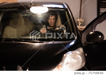 tired taxi driver parked the car in the garage, opened the door, sits sad in the car. 75749640