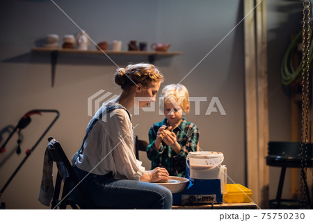a young woman potter helps a cute boy to make a gift for his mother out of clay. a young woman potter helps a cute boy to make a gift for his mother out of clay. 75750230