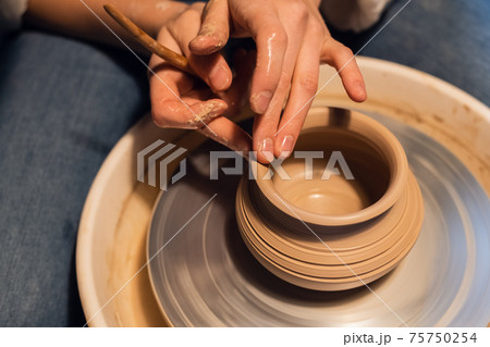 beautiful hands of a young girl potter in the process of sculpting a vase with clay and tools. 75750254