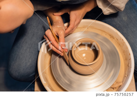 close-up of the hands of a potter when sculpting a vase from clay on a potter's wheel in the workshop. 75750257