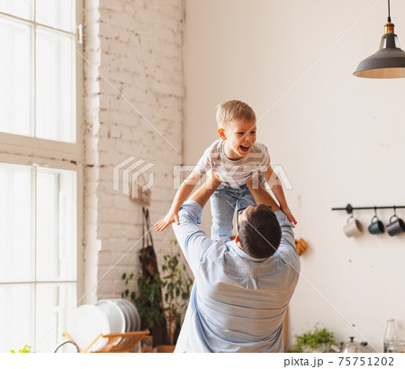 Anonymous father lifting cute son above head in kitchen Anonymous father lifting cute son above head in kitchen 75751202