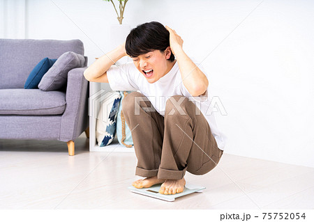 体重計に乗ってショックで頭をかかえる男性 75752054