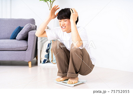 体重計に乗ってショックで頭をかかえる男性 75752055