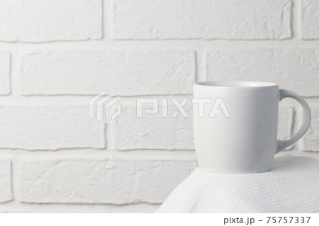 Household utensils, a white cup stands on a napkin against the background of a kitchen stone brick wall of a milky shade, the concept of clean dishes Household utensils, a white cup stands on a napkin against the background of a kitchen stone brick wall of a milky shade, the concept of clean dishes 75757337