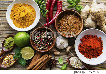 A selection of various colorful spices on a wooden table in bowls and spoons A selection of various colorful spices on a wooden table in bowls and spoons 75759202