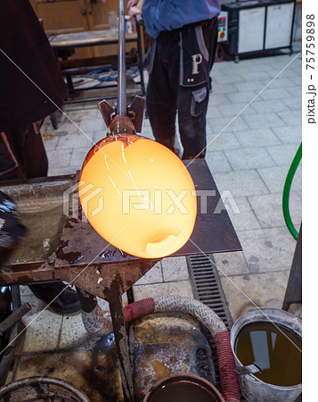 Worker in a glass studio. Talented glassblower is forming hot glass piece Worker in a glass studio. Talented glassblower is forming hot glass piece 75759898