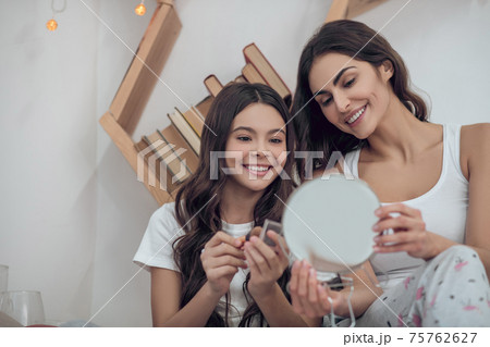 Cheerful mom showing mirror to smiling daughter Cheerful mom showing mirror to smiling daughter 75762627