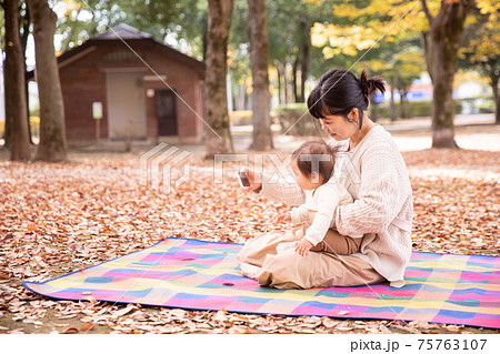 秋の公園でスマホで遊ぶ親子 75763107