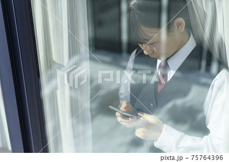 窓辺でスマートフォンを見る中学生（外出自粛要請のイメージ） 75764396
