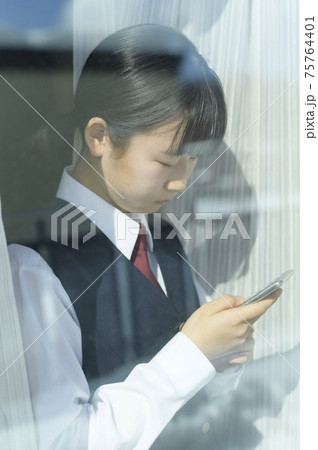 窓辺でスマートフォンを見る中学生(外出自粛要請のイメージ) 窓辺でスマートフォンを見る中学生(外出自粛要請のイメージ) 75764401
