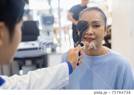 Middle aged asian woman examining close one eye to test vision from eye specialist doctor. Middle aged asian woman examining close one eye to test vision from eye specialist doctor. 75764738