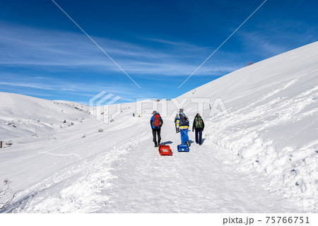 Hikers with Rucksacks and Bobsleighs on a Snowy path on Lessinia Plateau - Veneto Italy 75766751