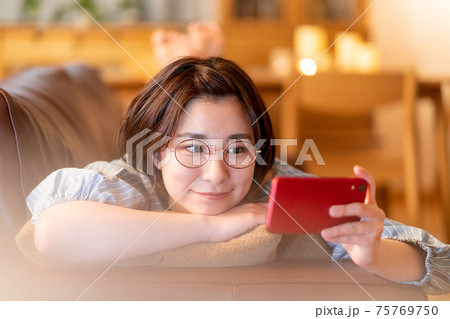 夜自宅のリビングのソファでスマホを見る若い女性 夜自宅のリビングのソファでスマホを見る若い女性 75769750