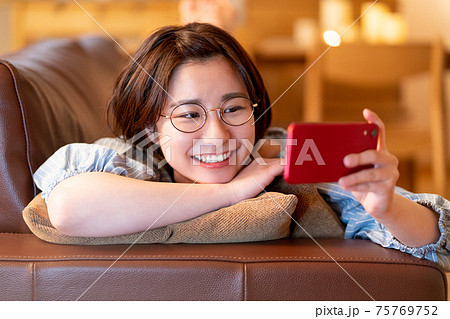 夜自宅のリビングのソファでスマホを見る若い女性 夜自宅のリビングのソファでスマホを見る若い女性 75769752