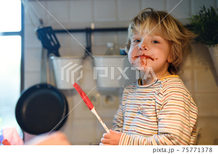 Small boy indoors in kitchen at home, helping with cooking. 75771378