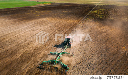 Aerial View. Tractor Plowing Field. Beginning Of Agricultural Spring Season. Cultivator Pulled By A Tractor In Countryside Rural Field Landscape. Dust Rises From Under Plows Aerial View. Tractor Plowing Field. Beginning Of Agricultural Spring Season. Cultivator Pulled By A Tractor In Countryside Rural Field Landscape. Dust Rises From Under Plows 75773824