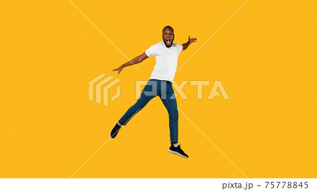 African Guy Jumping Shouting Looking At Camera, Yellow Background, Full-Length African Guy Jumping Shouting Looking At Camera, Yellow Background, Full-Length 75778845