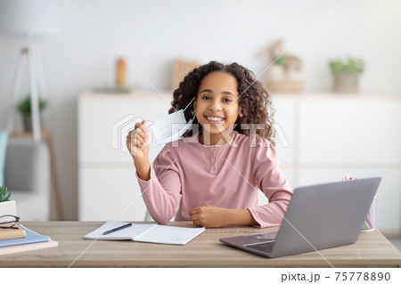 Remote education during lockdown. Black girl wearing medical face mask studying at home on laptop 75778890