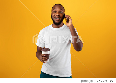 Guy Talking On Cellphone Holding Paper Coffee Cup, Yellow Background Guy Talking On Cellphone Holding Paper Coffee Cup, Yellow Background 75779135