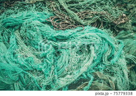 Close up view pile of green nylon multi colorful bright fish nets with pieces of white corals and old ropes in fishing village. Still life background pattern. Hobby fishing concept. Copy space 75779338