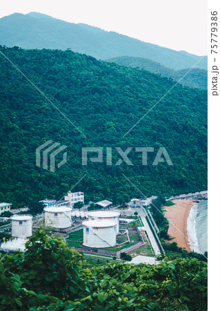 Oil loading terminal with large storage tanks near Sea port. Nature evening dusk, forested mountain background, boats. Business commercial trade fuel energy industry, environment ecology concept Oil loading terminal with large storage tanks near Sea port. Nature evening dusk, forested mountain background, boats. Business commercial trade fuel energy industry, environment ecology concept 75779386