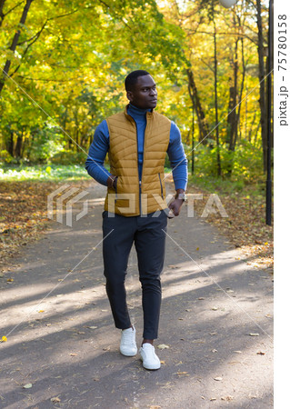Cheerful african american young man in stylish clothes walks in autumn park on sunny warm autumn day. Concept of weekend and outdoor recreation 75780158