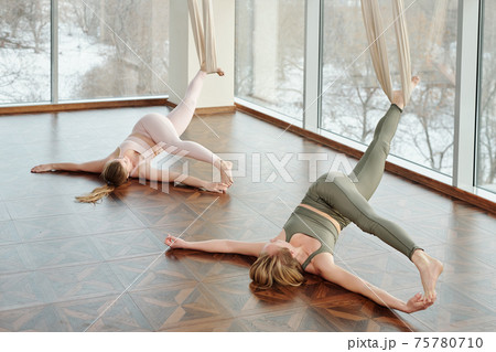 Young active women practicing fly yoga in gym with their legs stretched and hands touching feet Young active women practicing fly yoga in gym with their legs stretched and hands touching feet 75780710