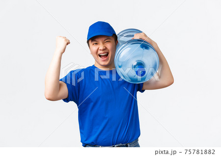Office and home delivery and employees concept. Cheerful asain male courier in blue uniform, carry bottle with clean water on shoulder, bring order to client and fist pump, best delivering company 75781882