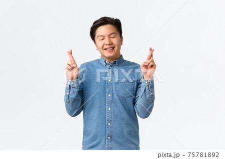 Smiling hopeful asian man feeling lucky, close eyse and grinning as awaiting for dream come true. Guy with braces cross fingers good luck, praying, asking god favour, standing white background Smiling hopeful asian man feeling lucky, close eyse and grinning as awaiting for dream come true. Guy with braces cross fingers good luck, praying, asking god favour, standing white background 75781892