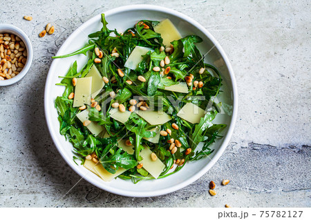 Arugula and parmesan salad with pine nuts in white bowl, top view. Italian cuisine concept. 75782127