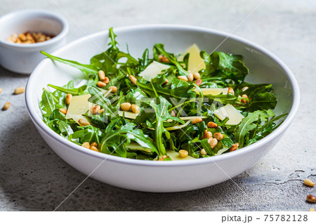Arugula and parmesan salad with pine nuts in white bowl. Italian cuisine concept. 75782128