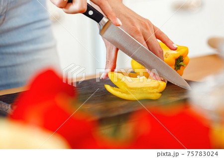 Woman cuts yellow bell pepper for salad on wooden table Woman cuts yellow bell pepper for salad on wooden table 75783024