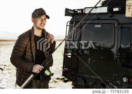 Young fisherman standing near his car and holding fishing equipment 75783150