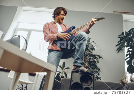 Young man plays guitar and sings a song at home with electric guitar Young man plays guitar and sings a song at home with electric guitar 75783327