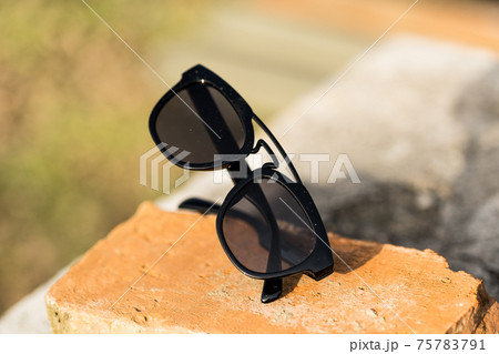 Sunglasses with black lenses and black frame shoot outside in a sunny day closeup . Selective focus Sunglasses with black lenses and black frame shoot outside in a sunny day closeup . Selective focus 75783791