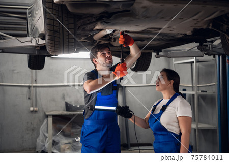 Techie and mechanic inspect car with torch Techie and mechanic inspect car with torch 75784011