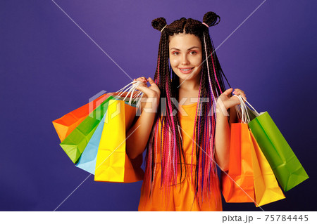 Young caucasian woman teenager holding a pile of colorful shopping bags against purple background 75784445