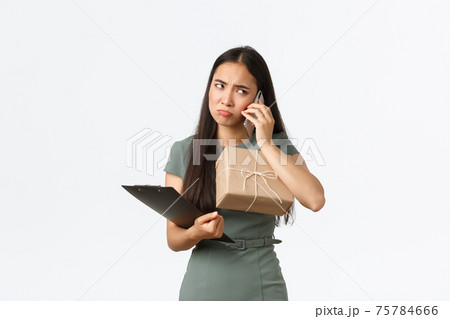 Upset pouting asian businesswoman holding clients package and clipboard with customer info, manage small business from home, talking with angry client, feeling sad about negative feedback 75784666