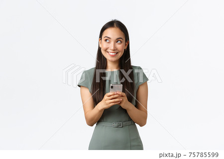 Small business owners, women entrepreneurs concept. Dreamy smiling stylish asian blogger, looking upper left corner thoughtful, creating content, thinking while texting message, using smartphone Small business owners, women entrepreneurs concept. Dreamy smiling stylish asian blogger, looking upper left corner thoughtful, creating content, thinking while texting message, using smartphone 75785599