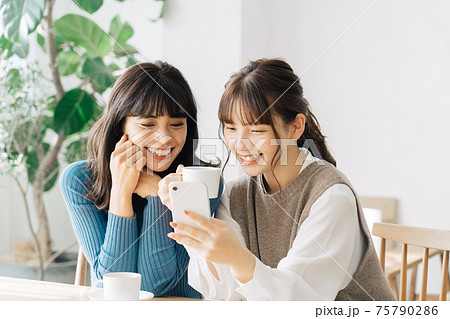 カフェでスマホを見る笑顔の女性2人組 75790286