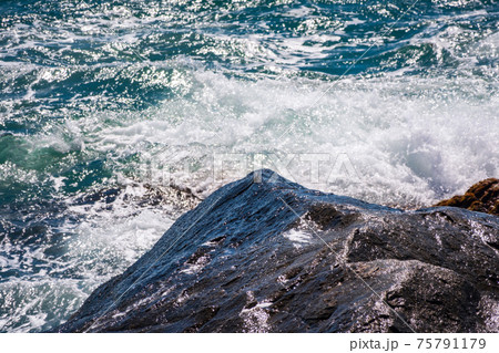Sea waves of dark water beat against the coastal rocks. An infinite number of splashes, drops of water and white foam are scattered. 75791179